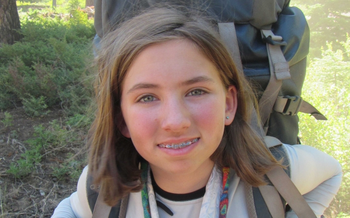 a young person wearing a backpack smiles at the camera